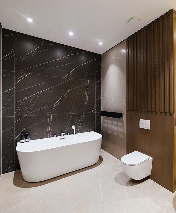 A freestanding tub with a toilet in a bath with large black tile wall