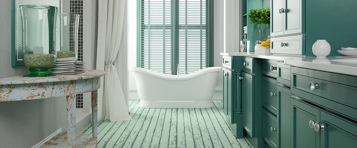A beautiful green bathroom with worn out wood floors and a green vanity