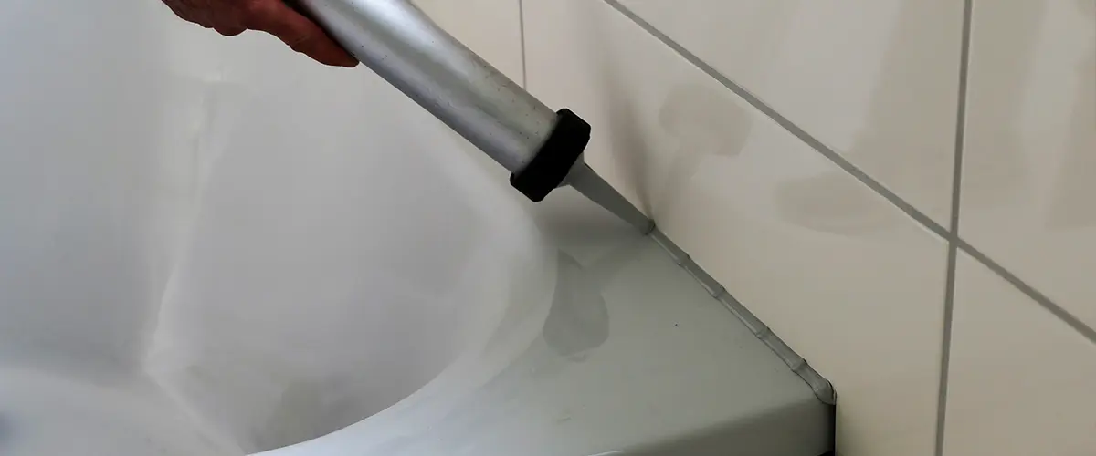 A contractor applying caulk and grout around a bath tub