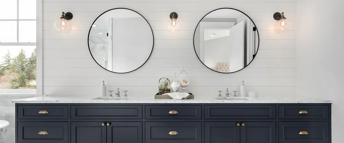 A navy blue double vanity with two round mirrors and light sconces