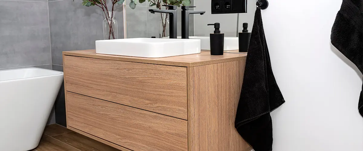 A simple wood vanity with no handles and black towels and soap dispenser