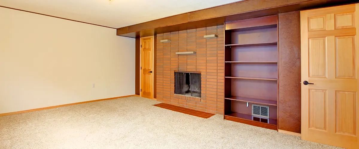 A finished basement with a brick fireplace and a carpet flooring