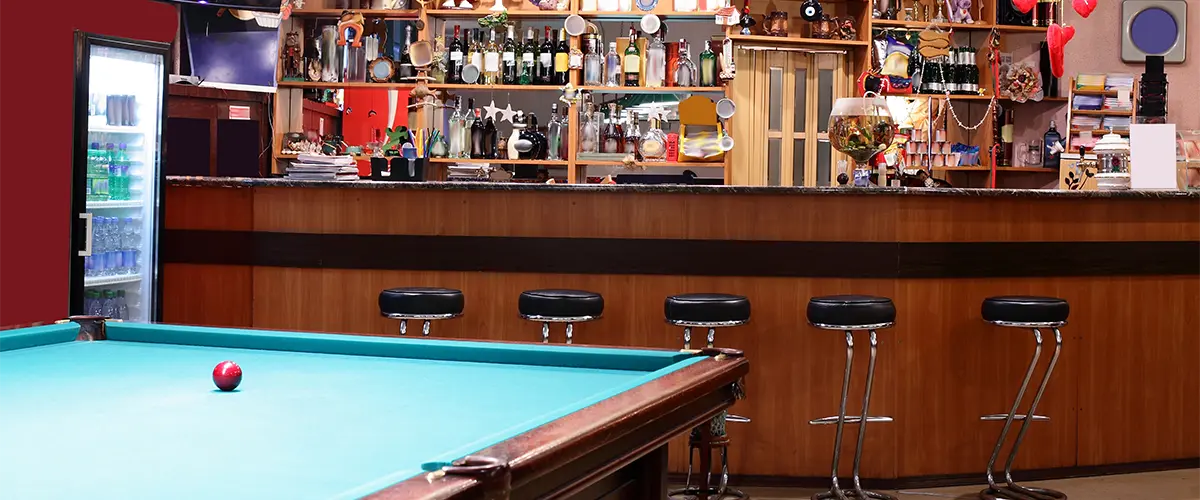 A man cave with a pool table and a large bar with stools