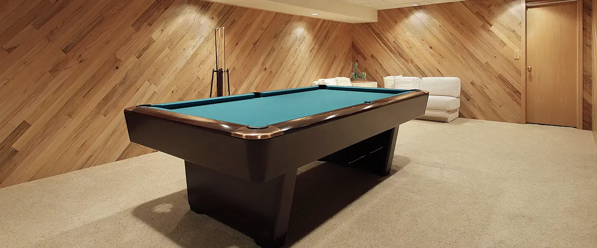 A pool table in a basement with carpet flooring